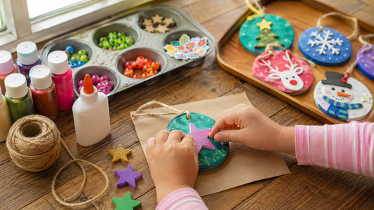 Child decorating a painted wooden disk ornament with a foam star at a craft table
