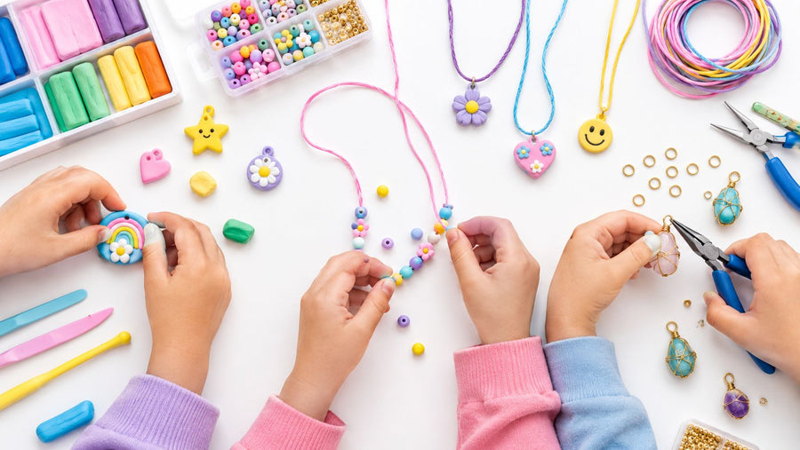 Children's hands making pendant necklaces: shaping a clay rainbow charm, threading beads onto cord, and wrapping wire around a stone with pliers.