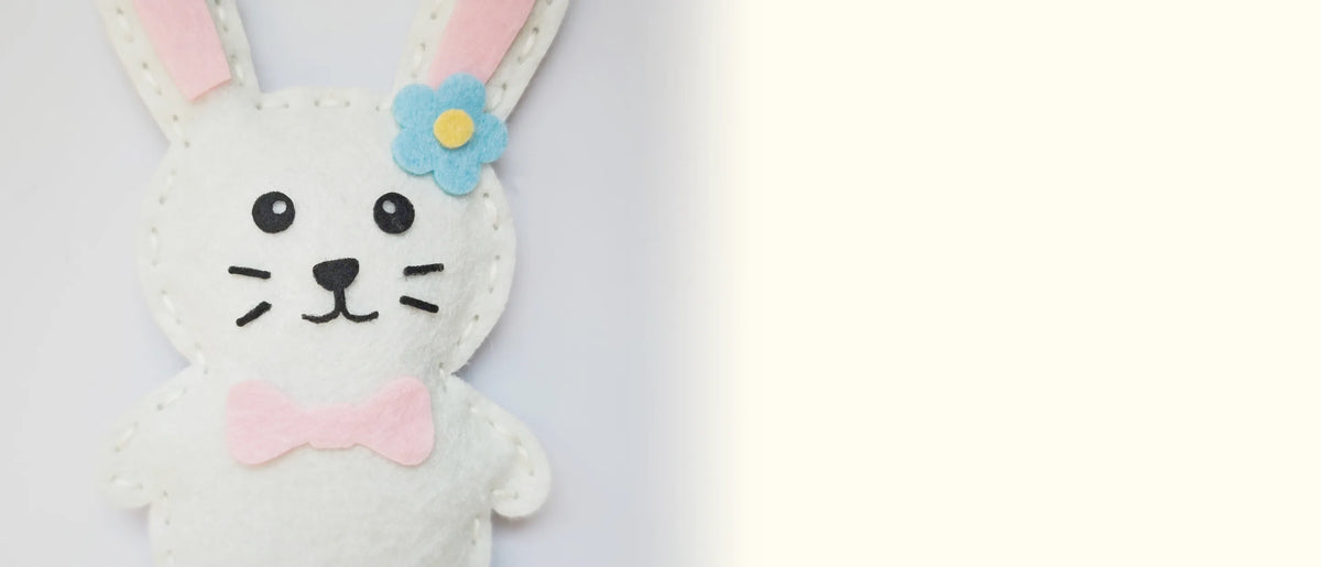 Finished felt bunny with long ears and a flower, on a pale gray background