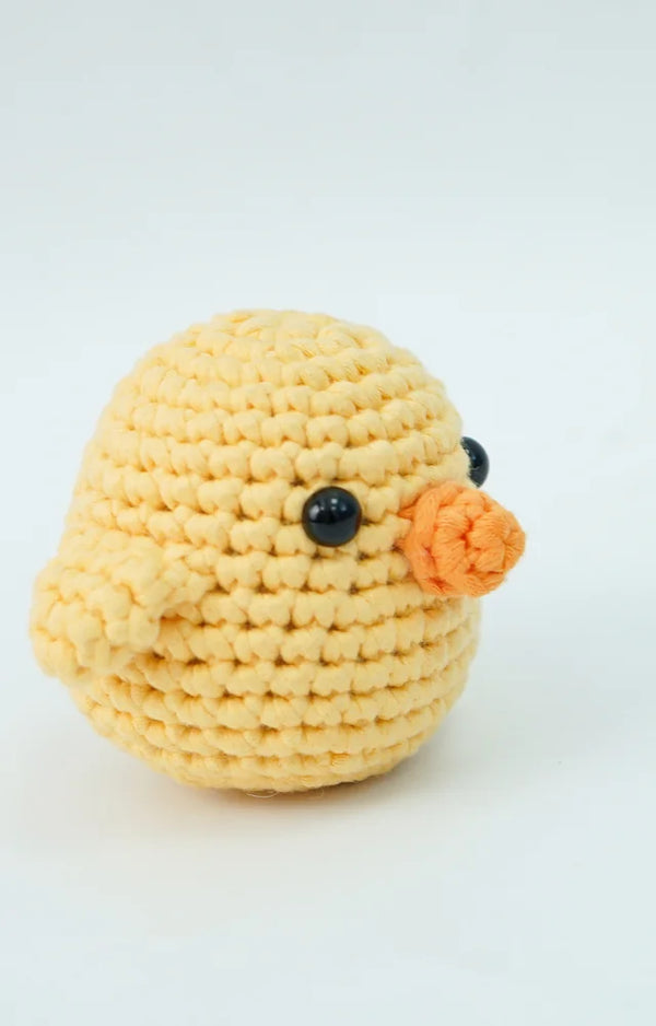 Three-quarter side view of the finished crocheted yellow chick with its orange beak