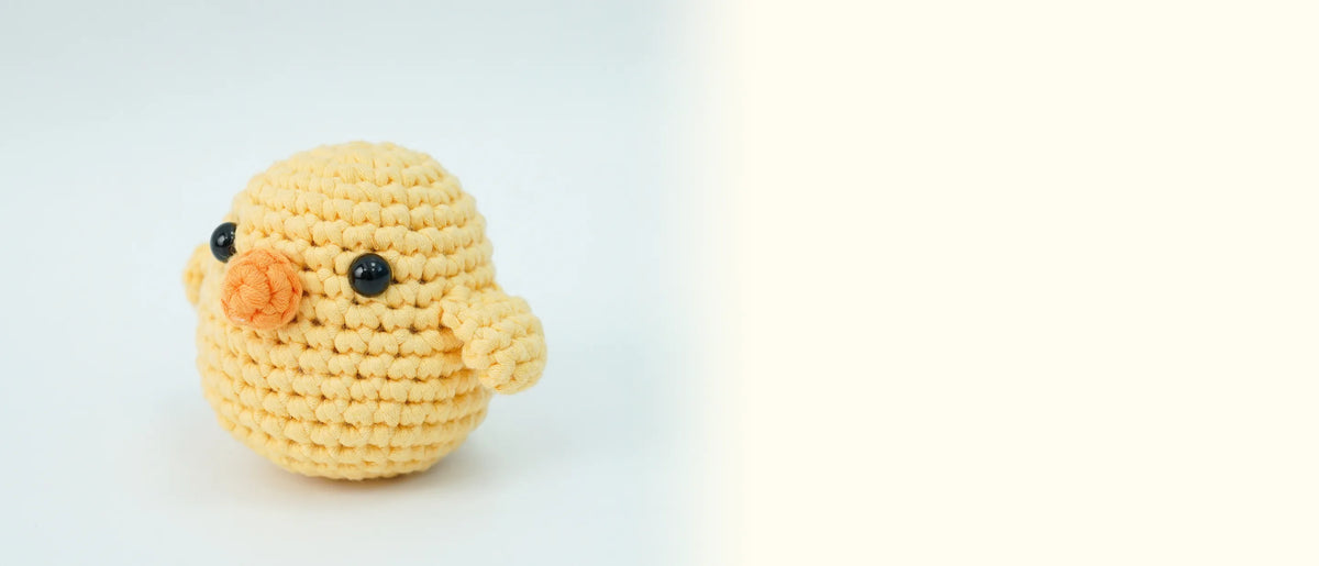 Three-quarter view of the finished crocheted yellow chick on a pale blue background