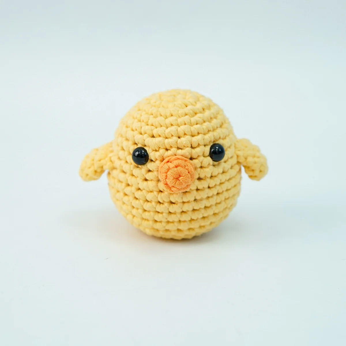 The finished crocheted yellow chick facing front with an orange beak and tiny wings out