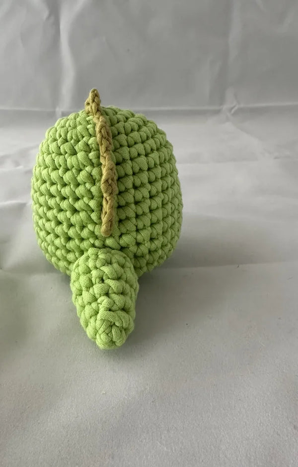 The crocheted green dinosaur seen from behind, showing the olive spikes on its spine and tail