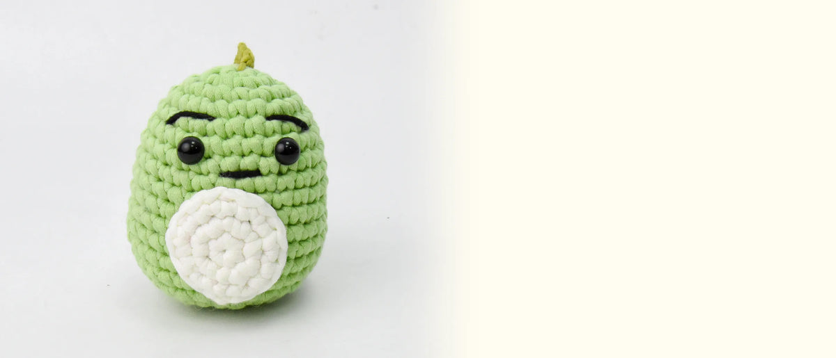 The finished crocheted green dinosaur facing the camera on a light gray background