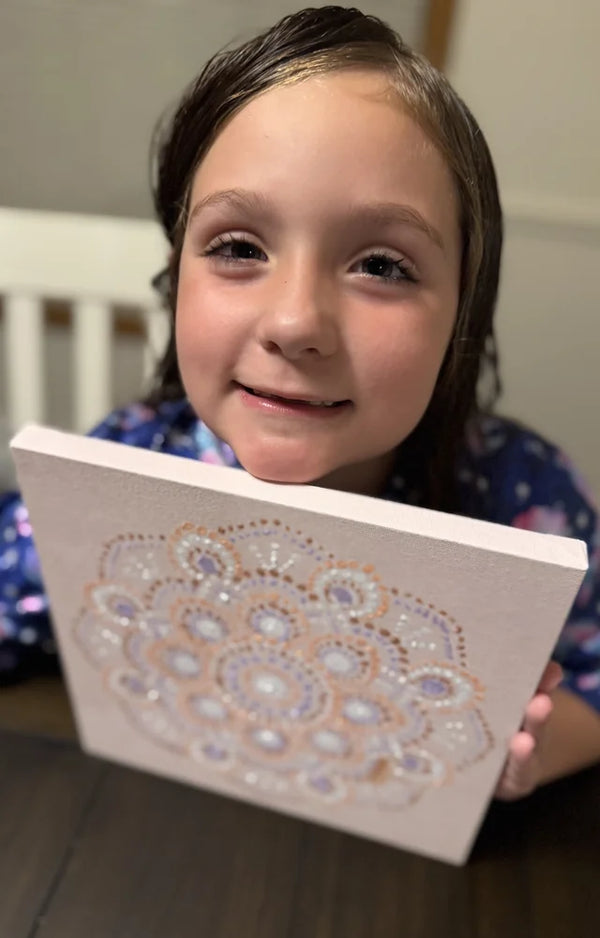 Smiling girl peeking over the top of her finished dot painting mandala canvas