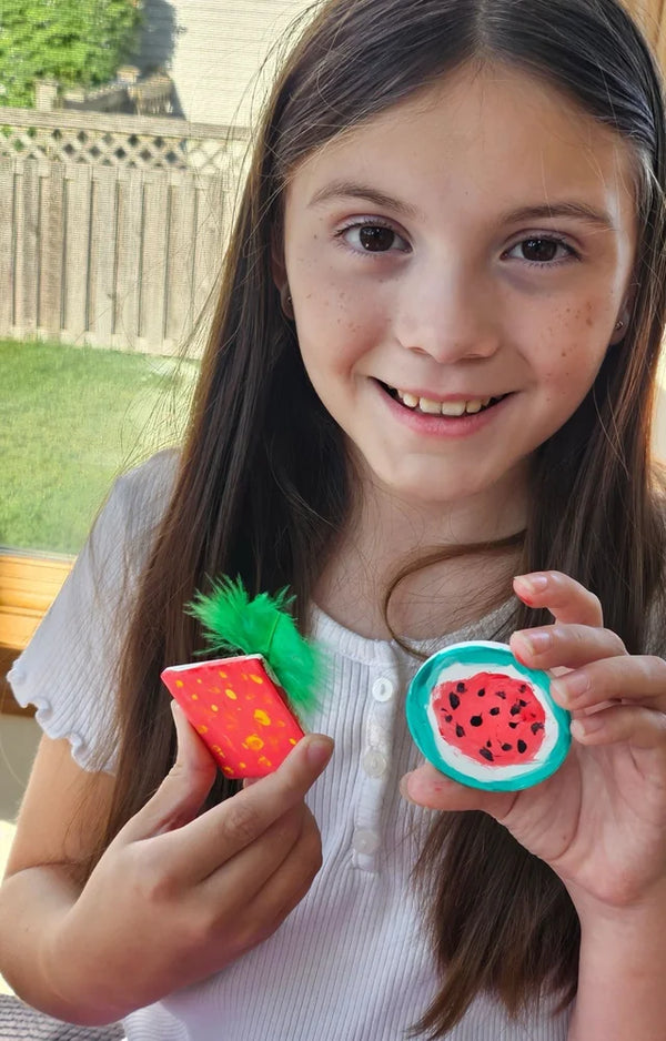 Smiling girl holding up the strawberry and watermelon magnets she painted herself