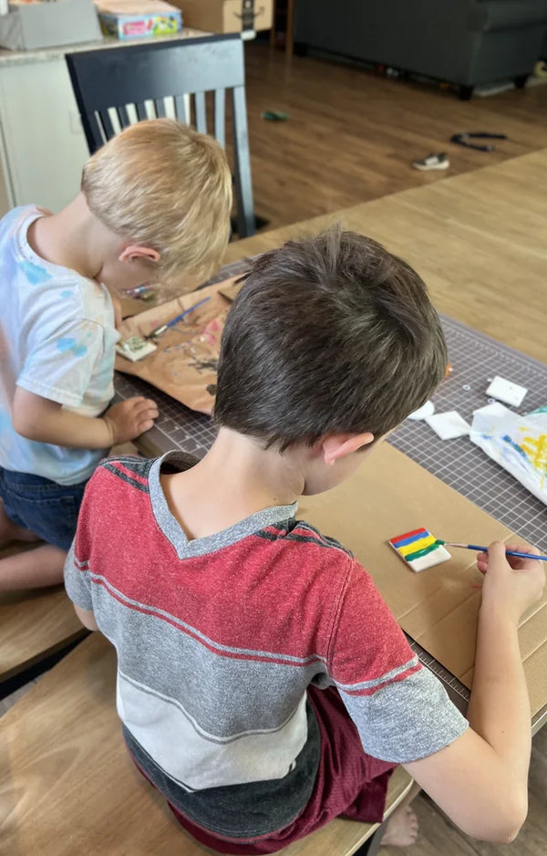 Two boys sitting side by side at a table painting their ceramic tile magnets
