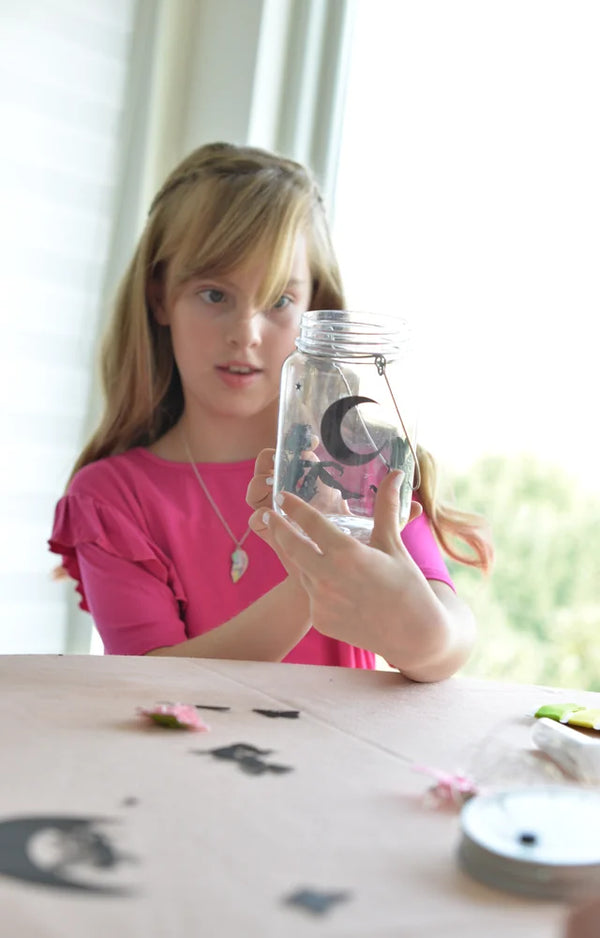 Girl holding up her finished fairy jar with a moon silhouette glowing inside it