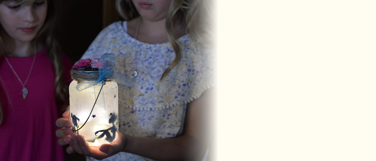 Two children holding a lit DIY fairy jar craft kit with decorative elements.