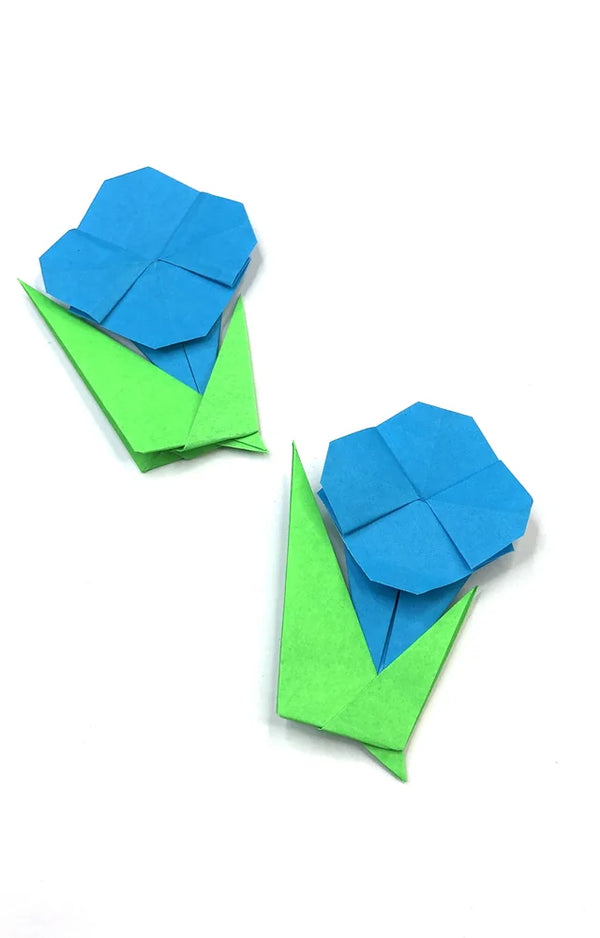 Two blue folded paper morning glory flowers on green paper stems with leaves, on a white background