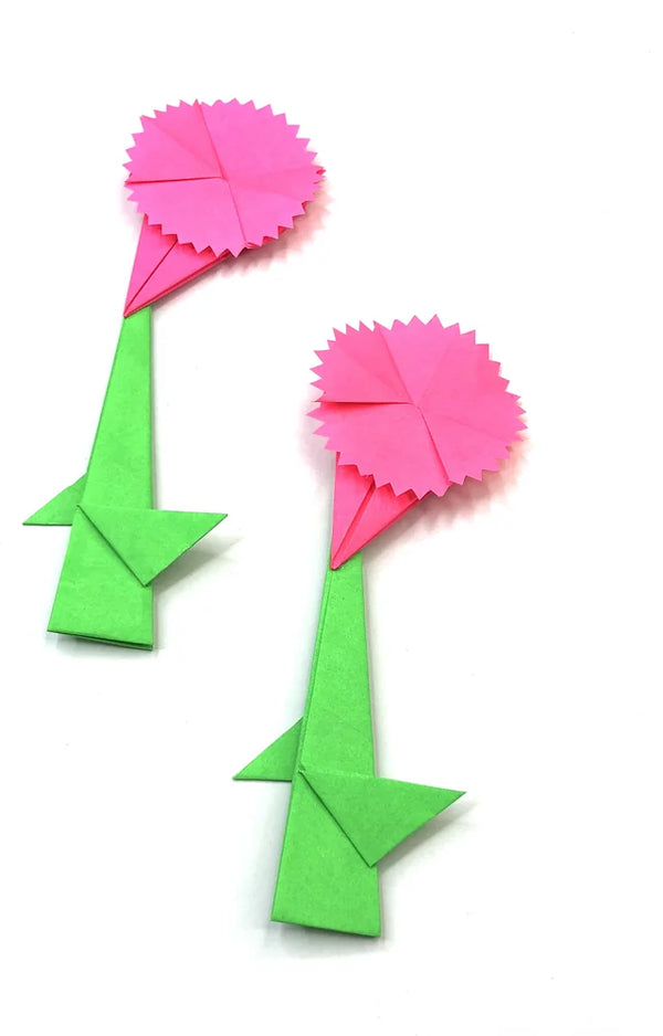 Two pink folded paper carnations with jagged petal edges on green paper stems and leaves