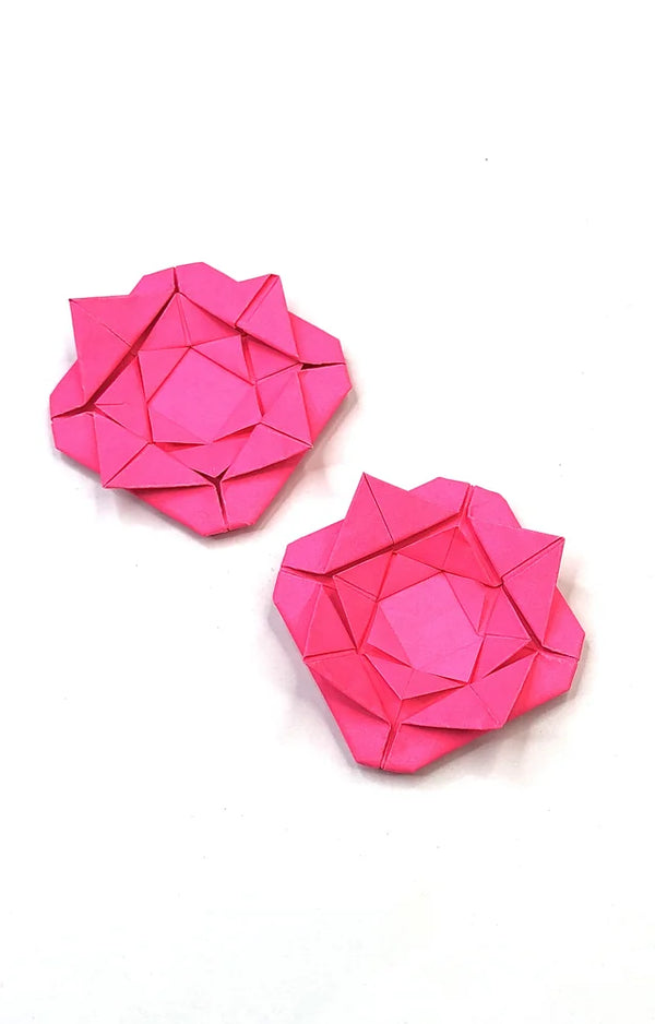 Two bright pink folded paper roses with layered petals lying on a plain white background