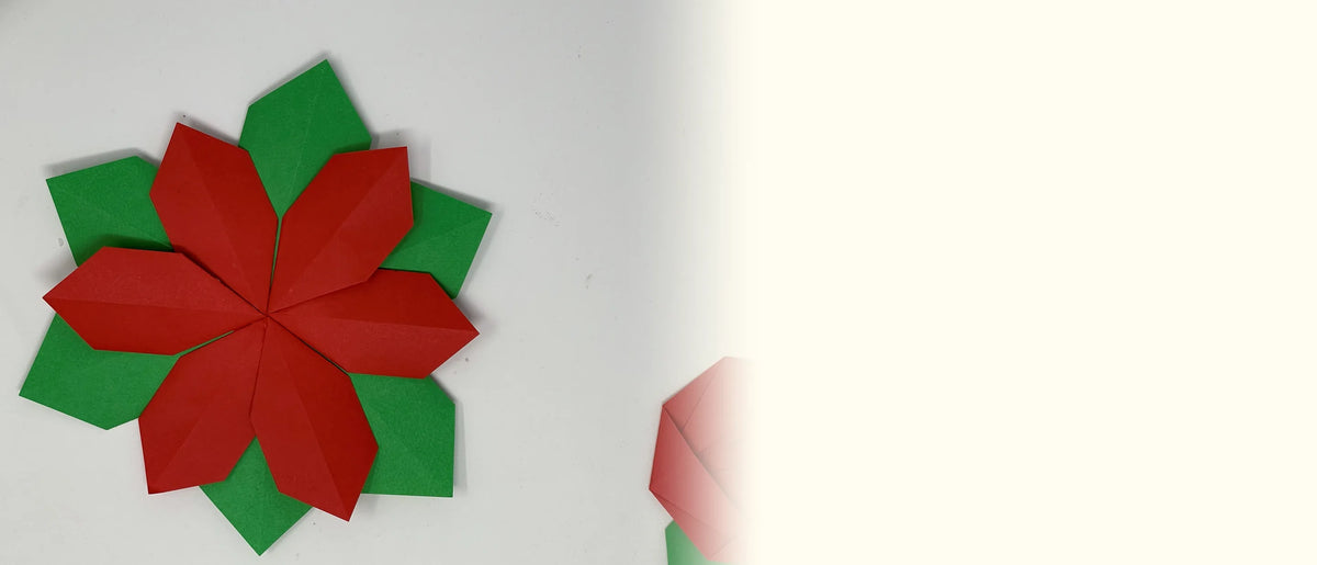 A red folded paper poinsettia with eight pointed petals set on a ring of green paper leaves
