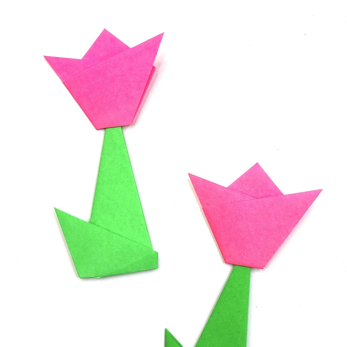 Two pink origami tulips on green folded paper stems with leaves, laid on a white background