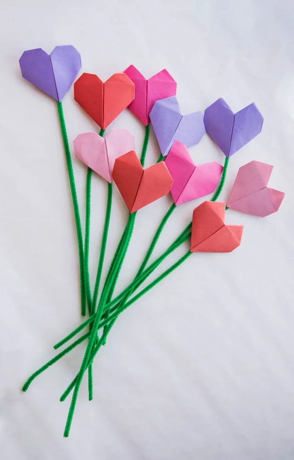 A bunch of pink, red and purple paper tulips on bendable green stems lying on a white sheet