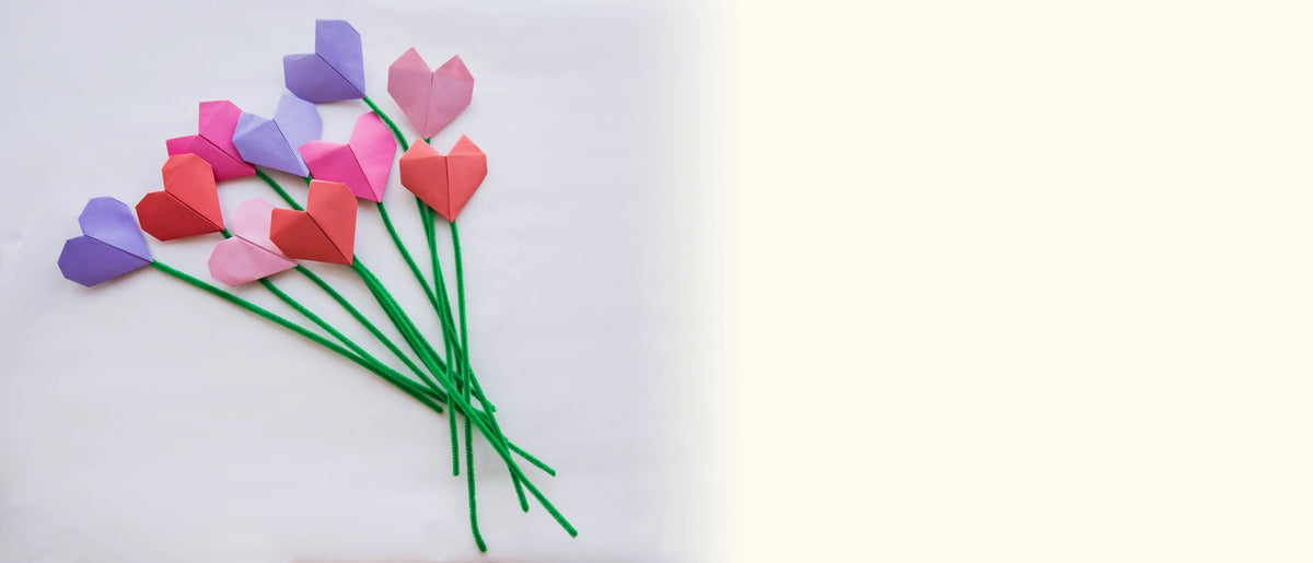 A bouquet of purple, pink and red paper tulips on long green stems laid on a white surface