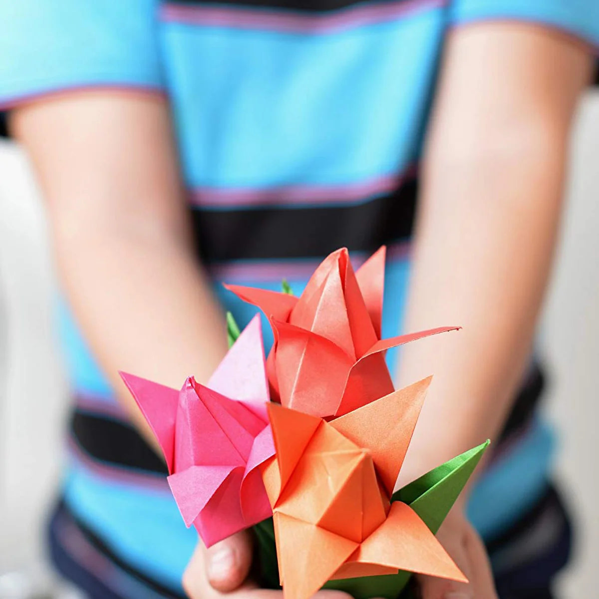 A child in a striped shirt holding a bouquet of pink, red and orange paper tulips toward the camera