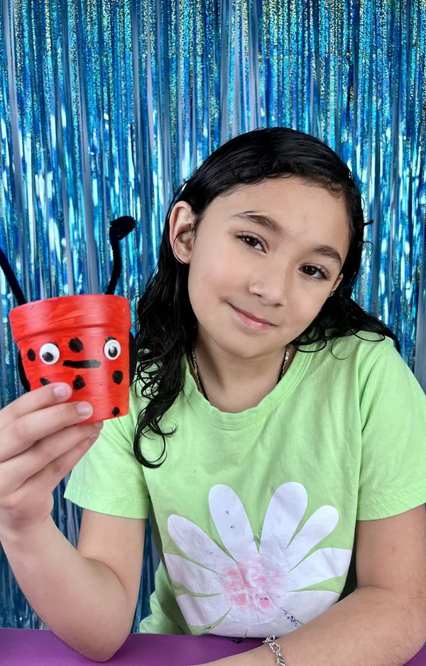 Girl holding up the ladybug flower pot she painted, with googly eyes and antennae