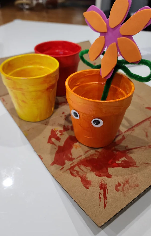 Painted orange flower pot with googly eyes and a foam flower on a chenille stem