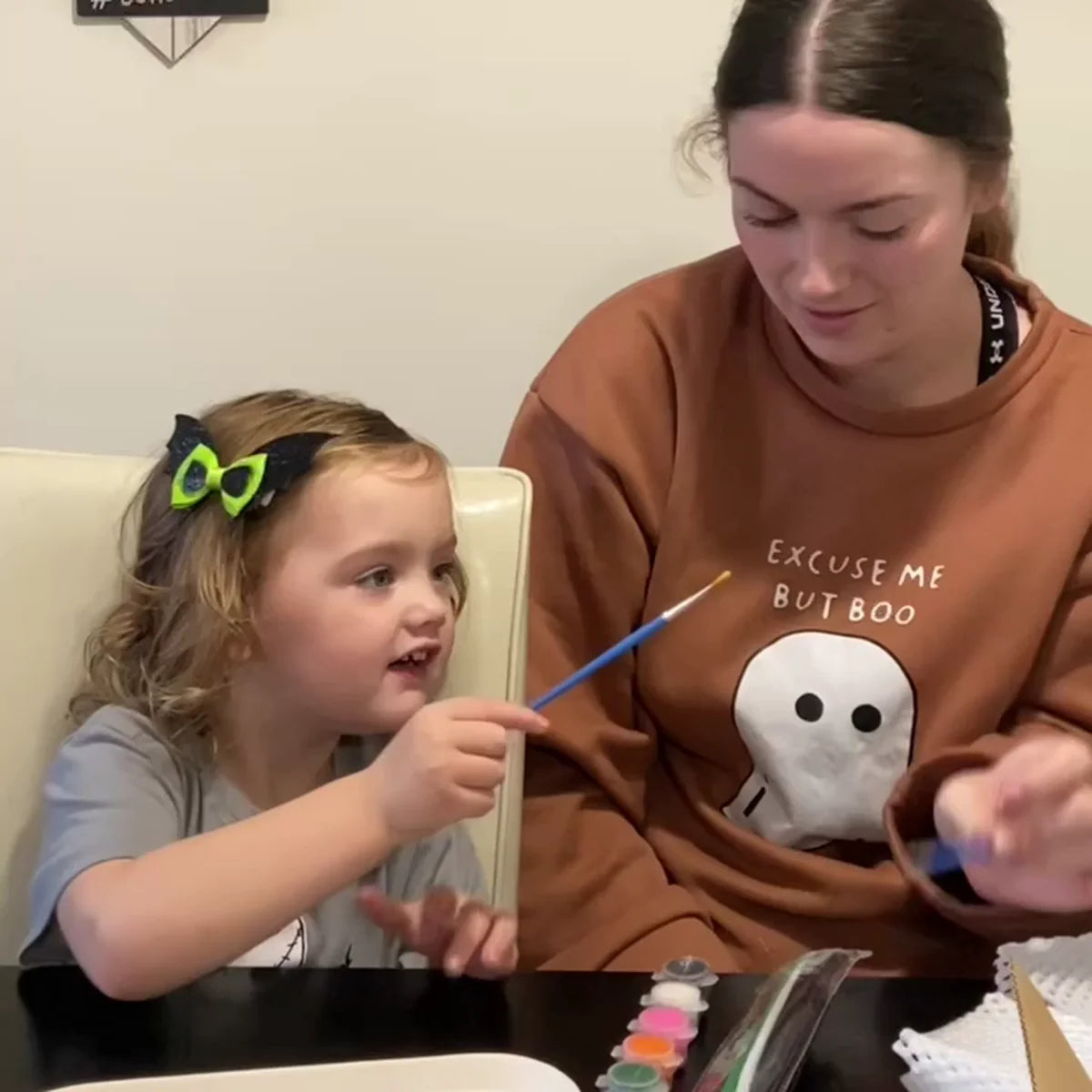 Young girl lifting her paintbrush beside her mother as they paint a flower pot