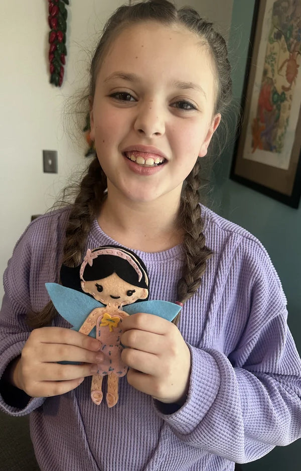 Girl in a purple sweater holding the felt fairy she stitched and stuffed