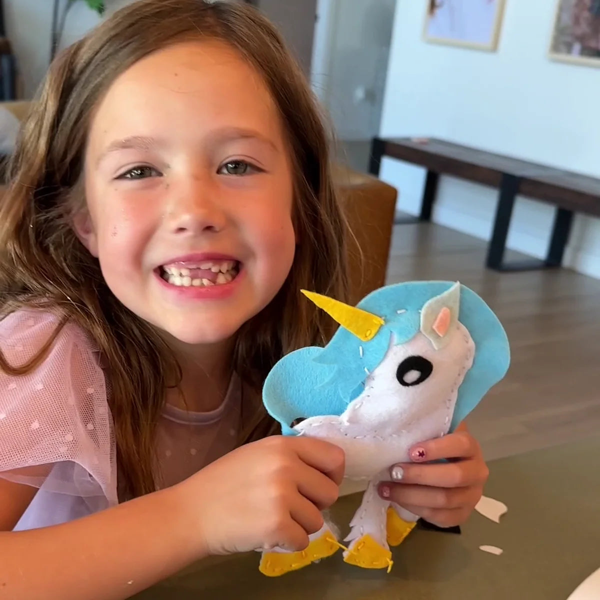Girl grinning as she holds up the finished felt unicorn she stitched herself