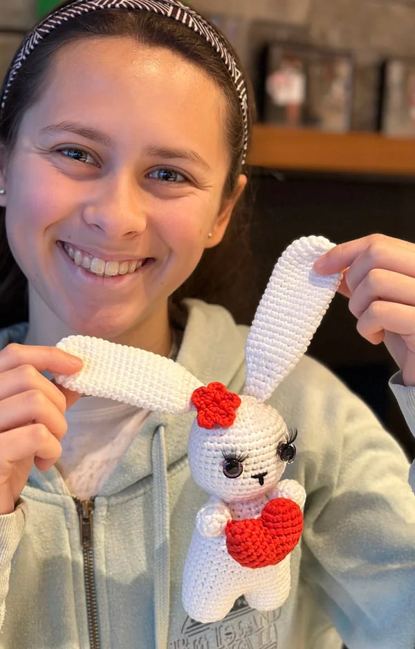 A teen holds the long ears of her finished crocheted white bunny up toward the camera