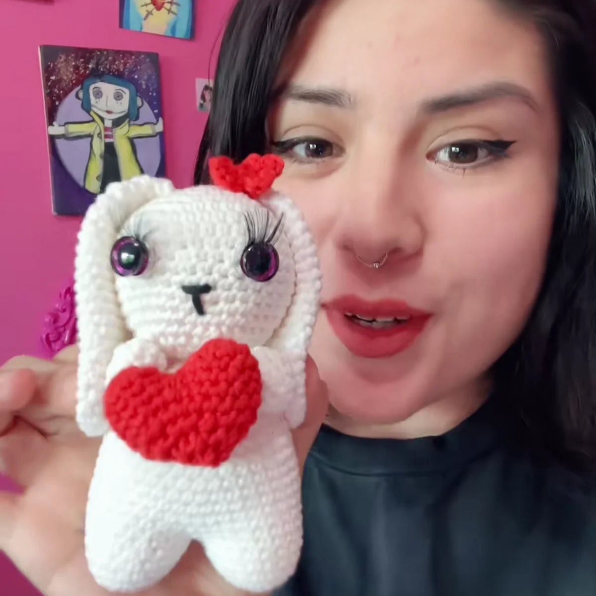 A creator holds her finished crocheted white bunny with a red heart beside her face