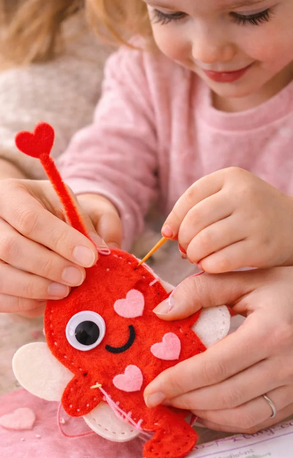 Child's hands stitching a red felt love bug with a grown-up helping