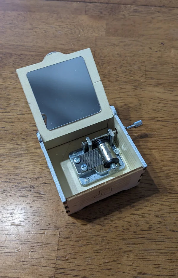 Finished wooden music box with its mirror lid open, showing the metal music box mechanism inside