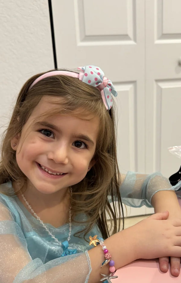 Girl in a blue dress smiling at her desk, wearing the mermaid charm bracelet she made