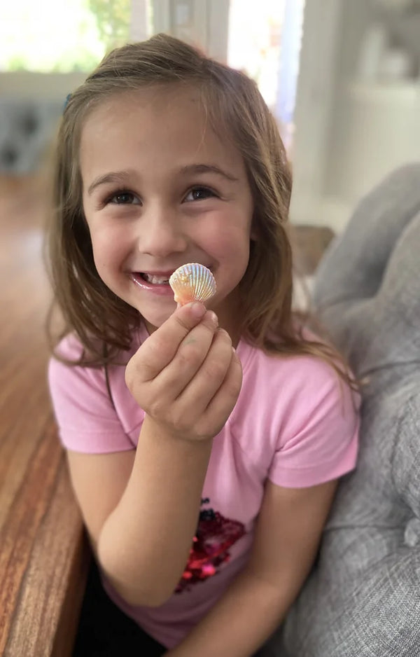 Girl grinning as she holds up a shell charm from her mermaid charm bracelet kit