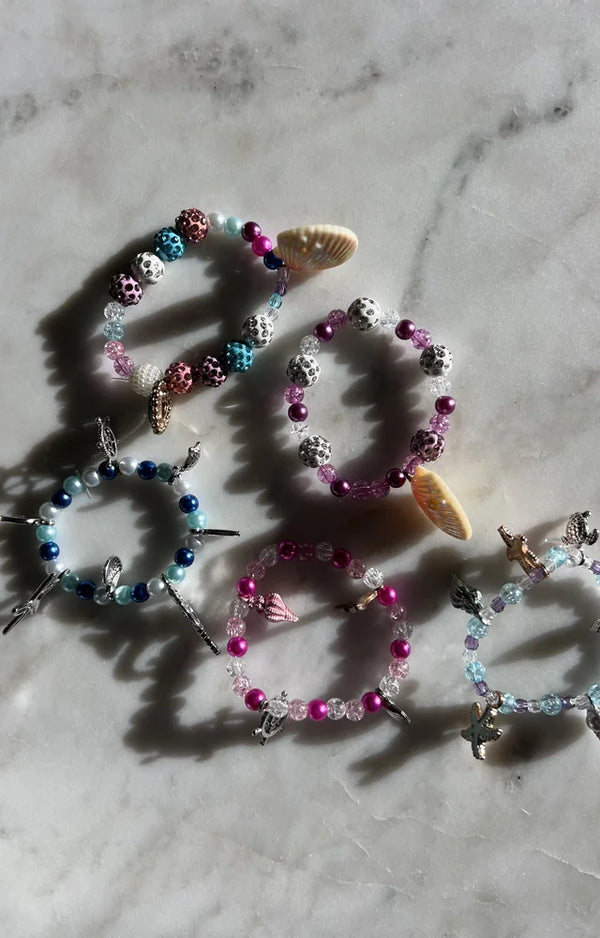 Five finished beaded mermaid charm bracelets laid side by side on a marble surface