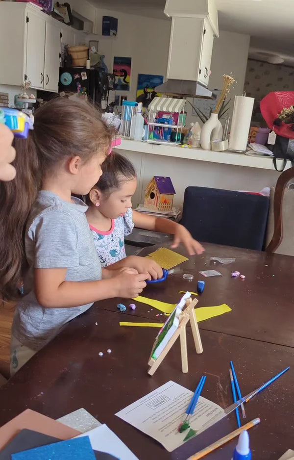 Two sisters decorate their mini canvases at the table, with easels and the instruction sheet in front