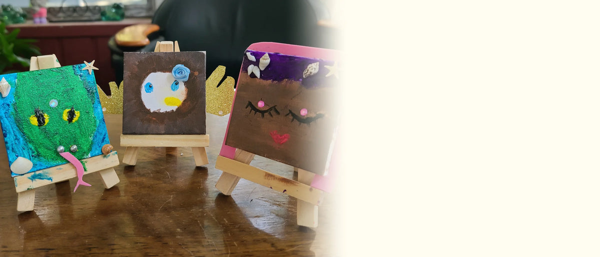 Three finished mini canvas characters standing on their little wooden easels on a wooden table