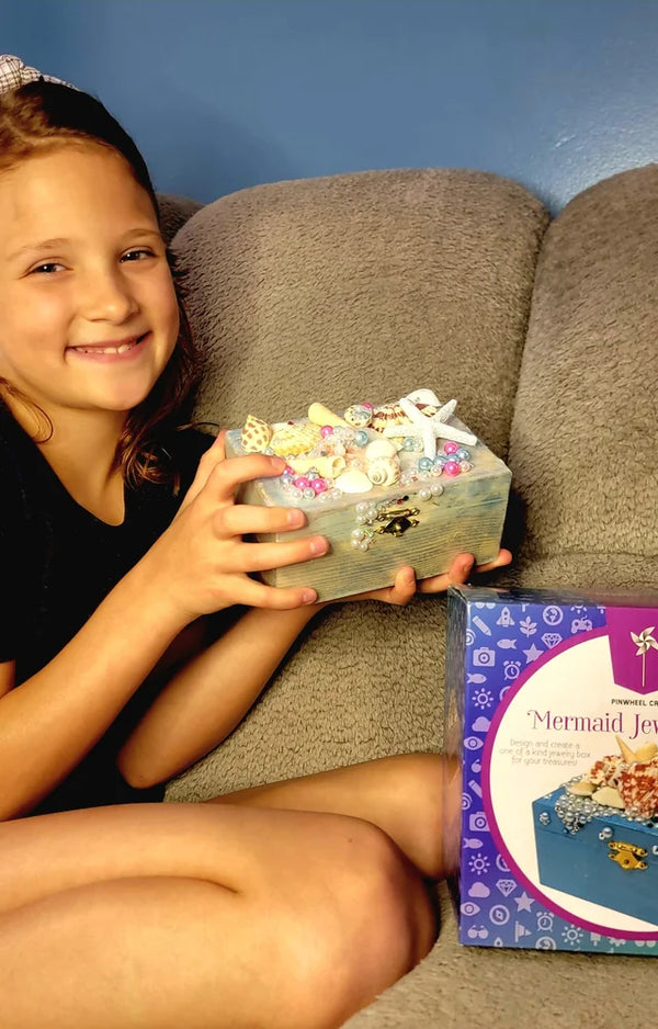 Girl on a sofa with her finished mermaid jewelry box and the kit box beside her