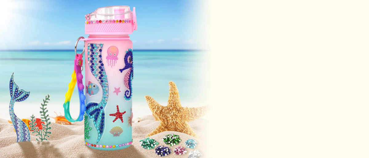 Decorated mermaid water bottle on the sand by the sea, beside a starfish and piles of gems