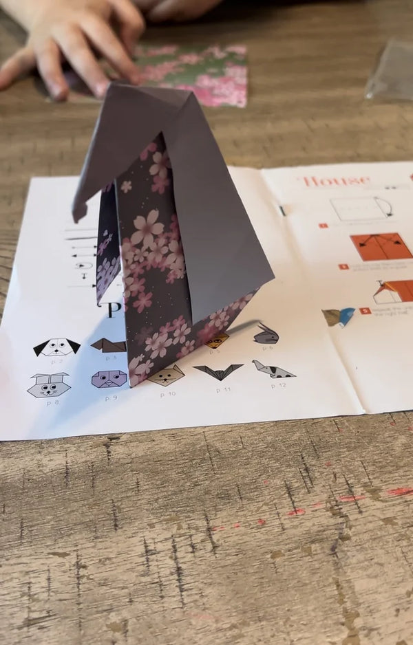 A patterned black and pink origami penguin standing on the open project book on a wooden table