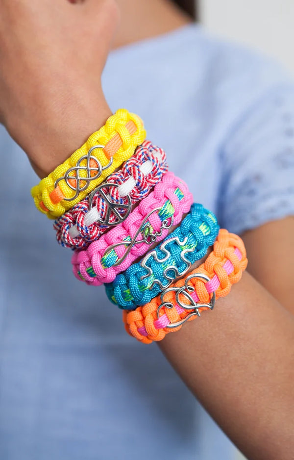 A wrist stacked with five colorful paracord bracelets, each with a different silver charm