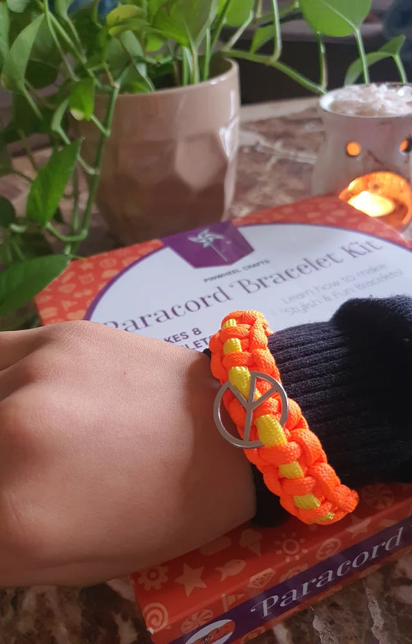 A wrist wearing an orange and yellow paracord bracelet with a charm, resting on the kit box