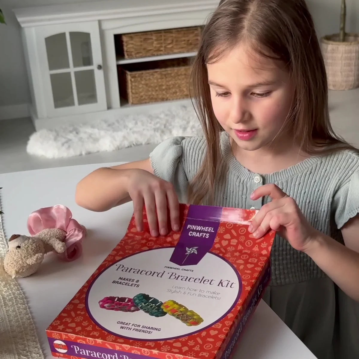 Girl smiling as she opens the Paracord Bracelet Kit box at a white table