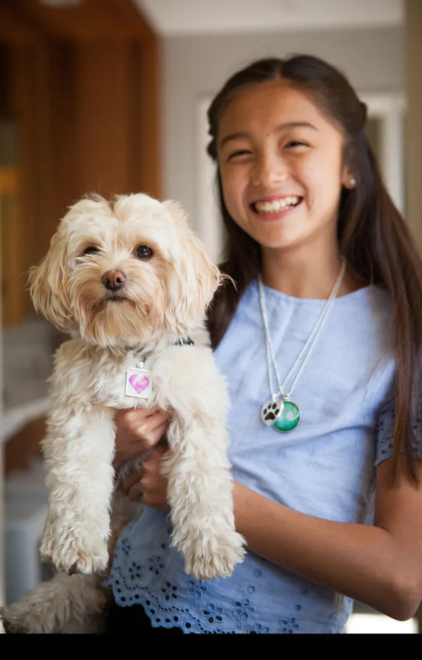 Girl holding her dog and wearing a pendant necklace she made