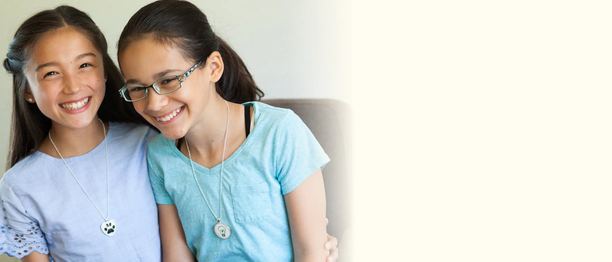 Two smiling girls wearing their handmade paw print and light bulb pendant necklaces