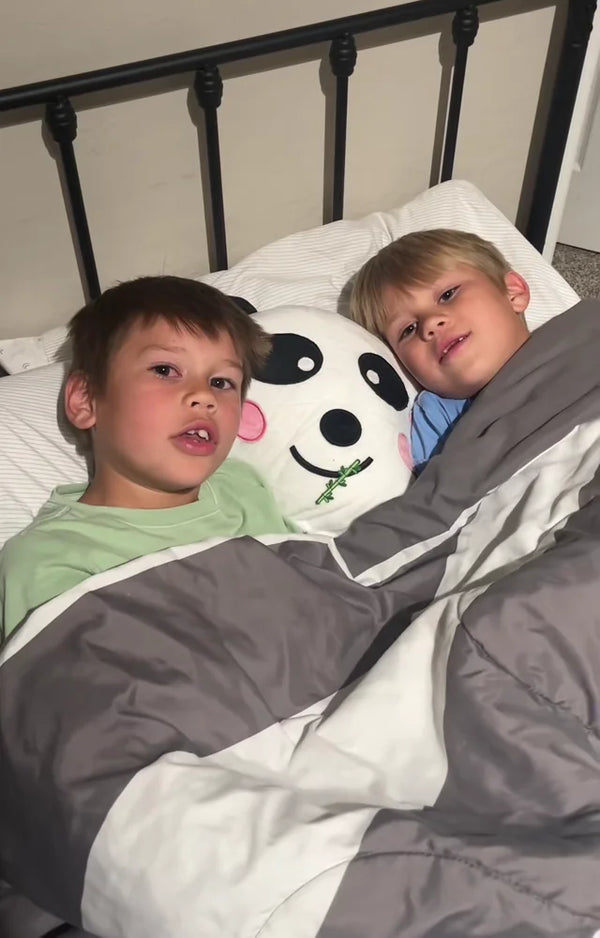 Two boys tucked into bed under the covers with the panda pillow they made together