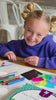 A girl paints ceramic tiles, adds glitter glue and shows off her finished fridge magnets