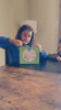 A girl opens the kit, builds the wooden T-rex at the table and makes it move with the controller