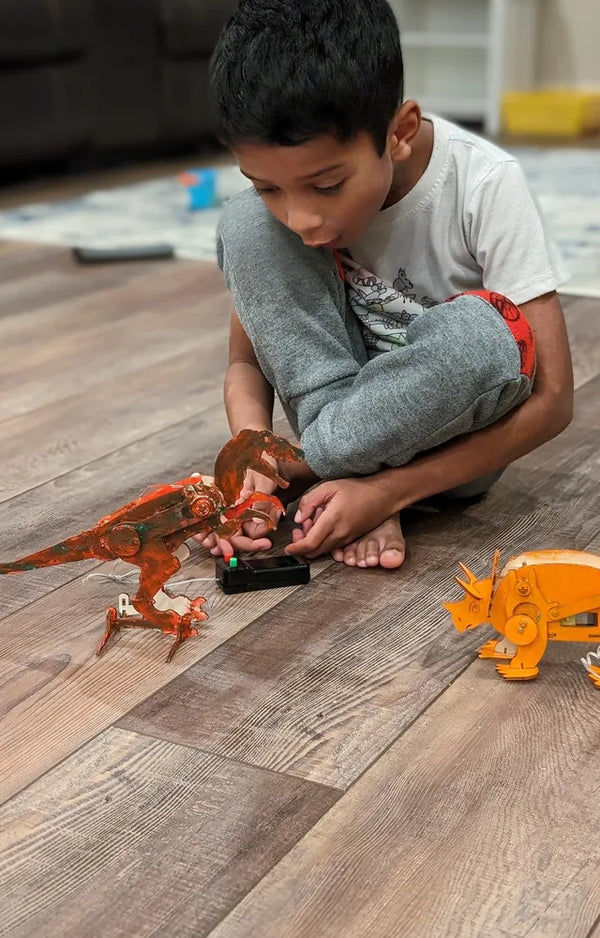 Boy on the floor running his painted T-rex and triceratops with their wired controllers