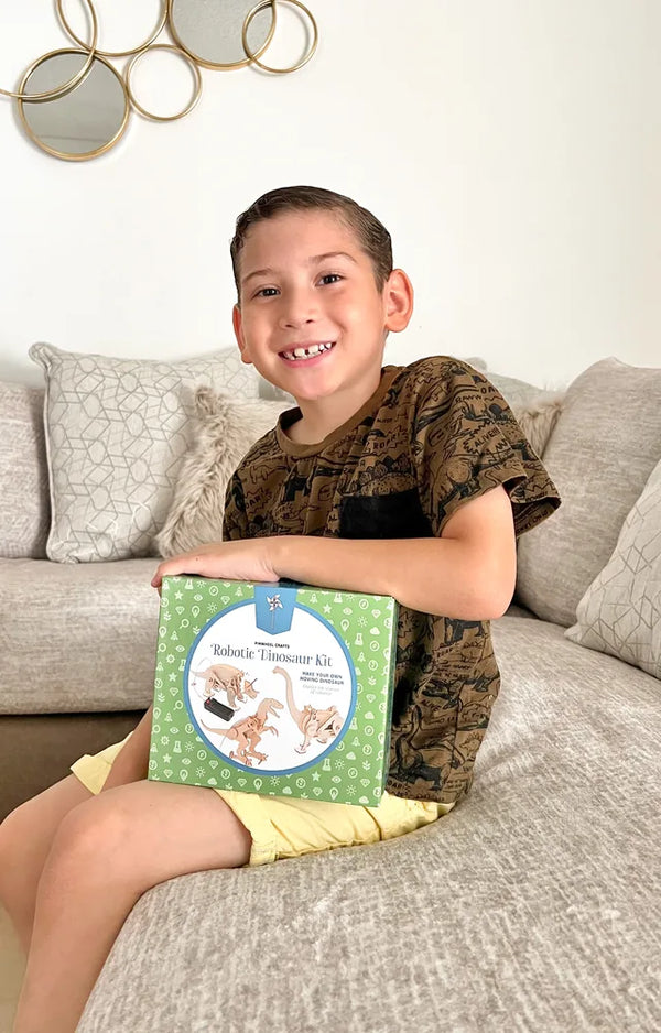 Smiling boy sitting on the couch hugging the Robotic Dinosaur Kit box on his lap