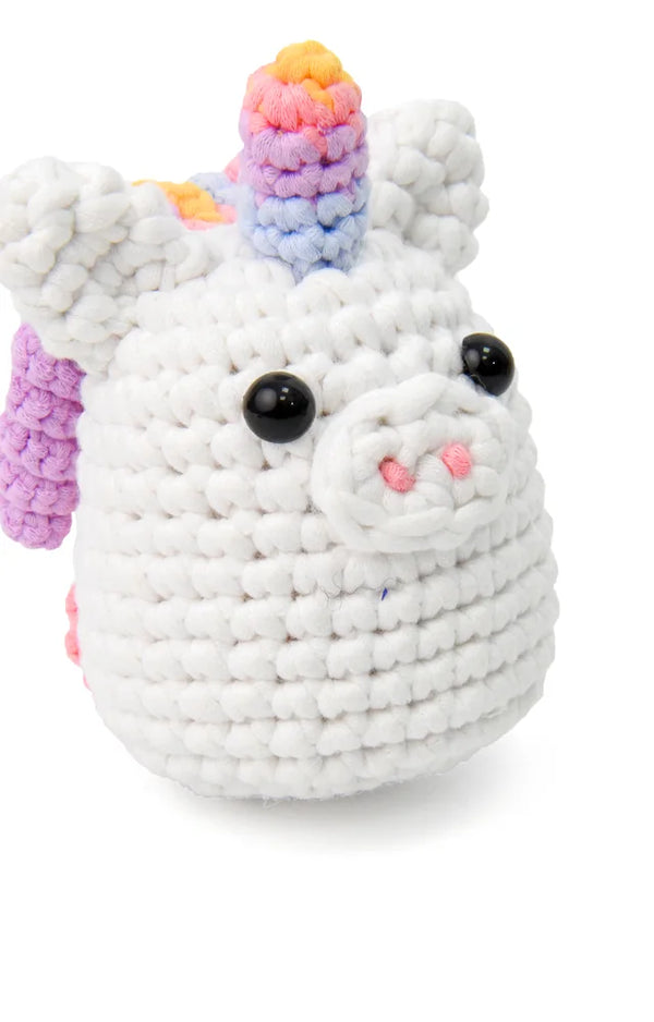 Three-quarter view of the finished crocheted rainbow unicorn sitting on a white background