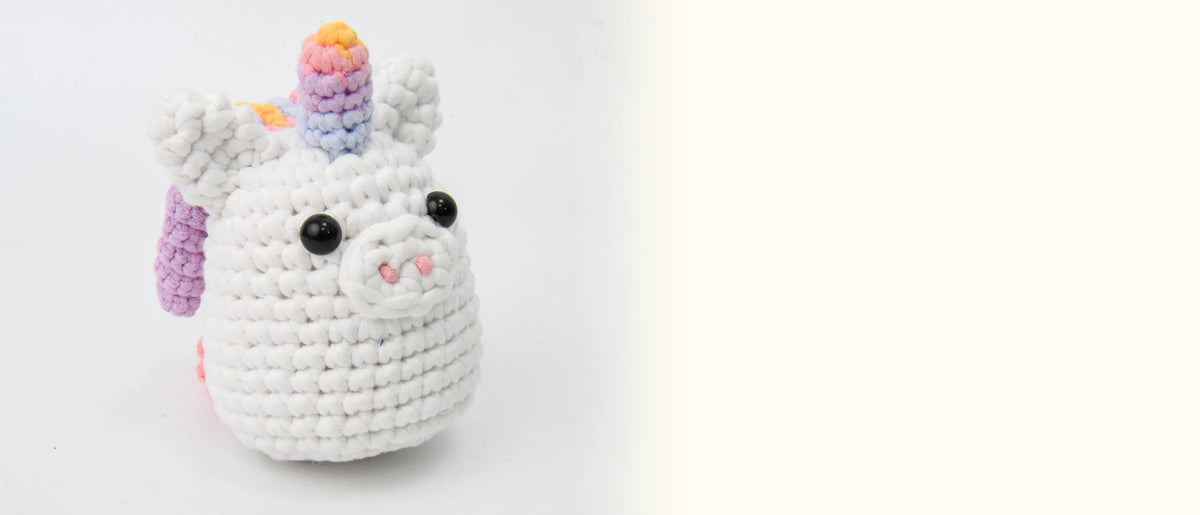 The finished crocheted rainbow unicorn with its rainbow horn and curly mane on a white background